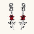 Gothic dangle earrings featuring silver serpent hooks with red enamel roses and metallic stems on white background.