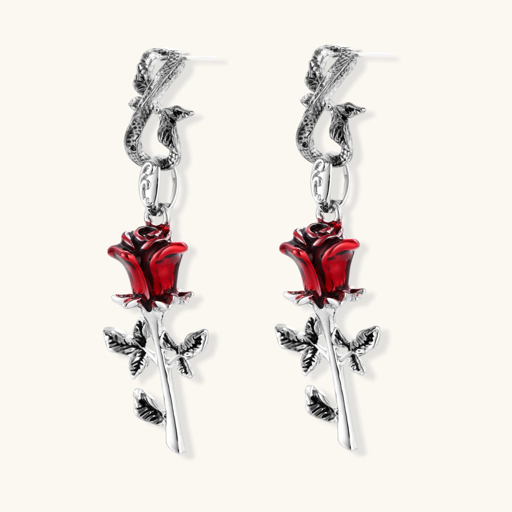 Gothic dangle earrings featuring silver serpent hooks with red enamel roses and metallic stems on white background.