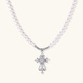 White pearl necklace with ornate silver cross pendant featuring zirconia crystals on cream background.