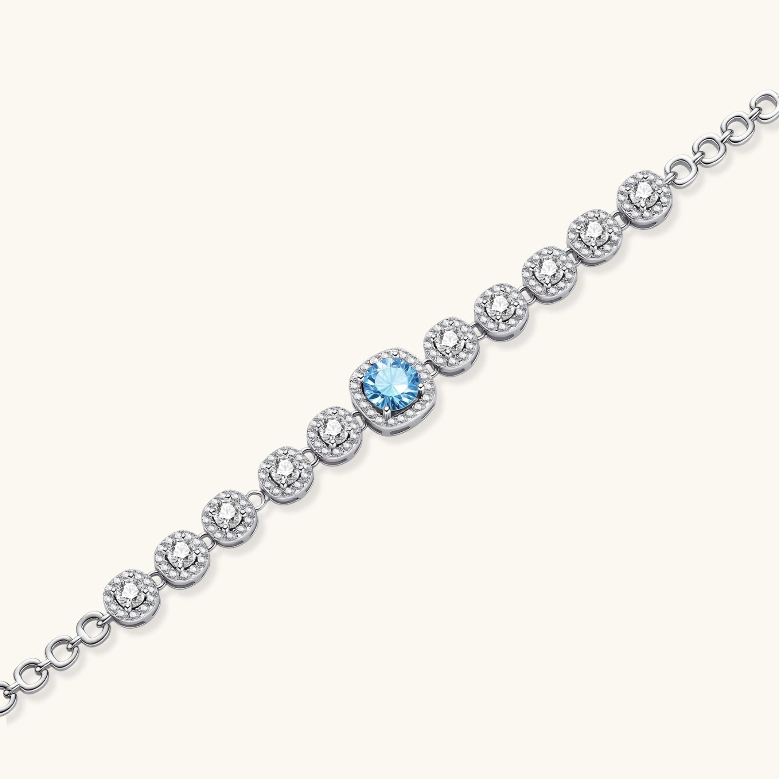 Sterling silver tennis bracelet with round halo-set moissanite stones and blue center stone on cream background.