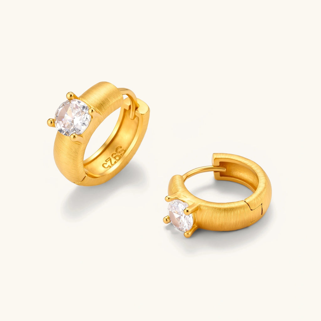18K gold-plated 925 silver huggie hoops with brushed finish and prong-set round CZ solitaire, stamped S925 inside.