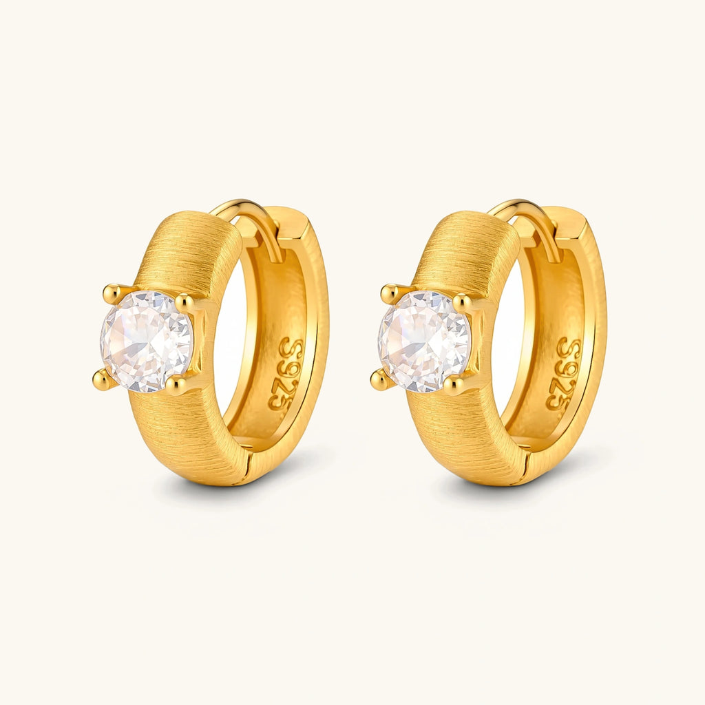 18K gold-plated 925 silver huggie hoops with brushed finish and prong-set round CZ solitaire, stamped S925 inside.